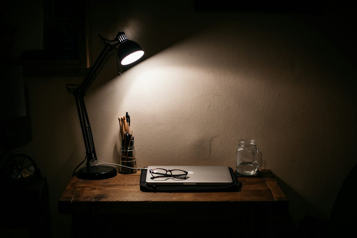 La nuit, une lampe de bureau éclaire un ordinateur resté fermé.